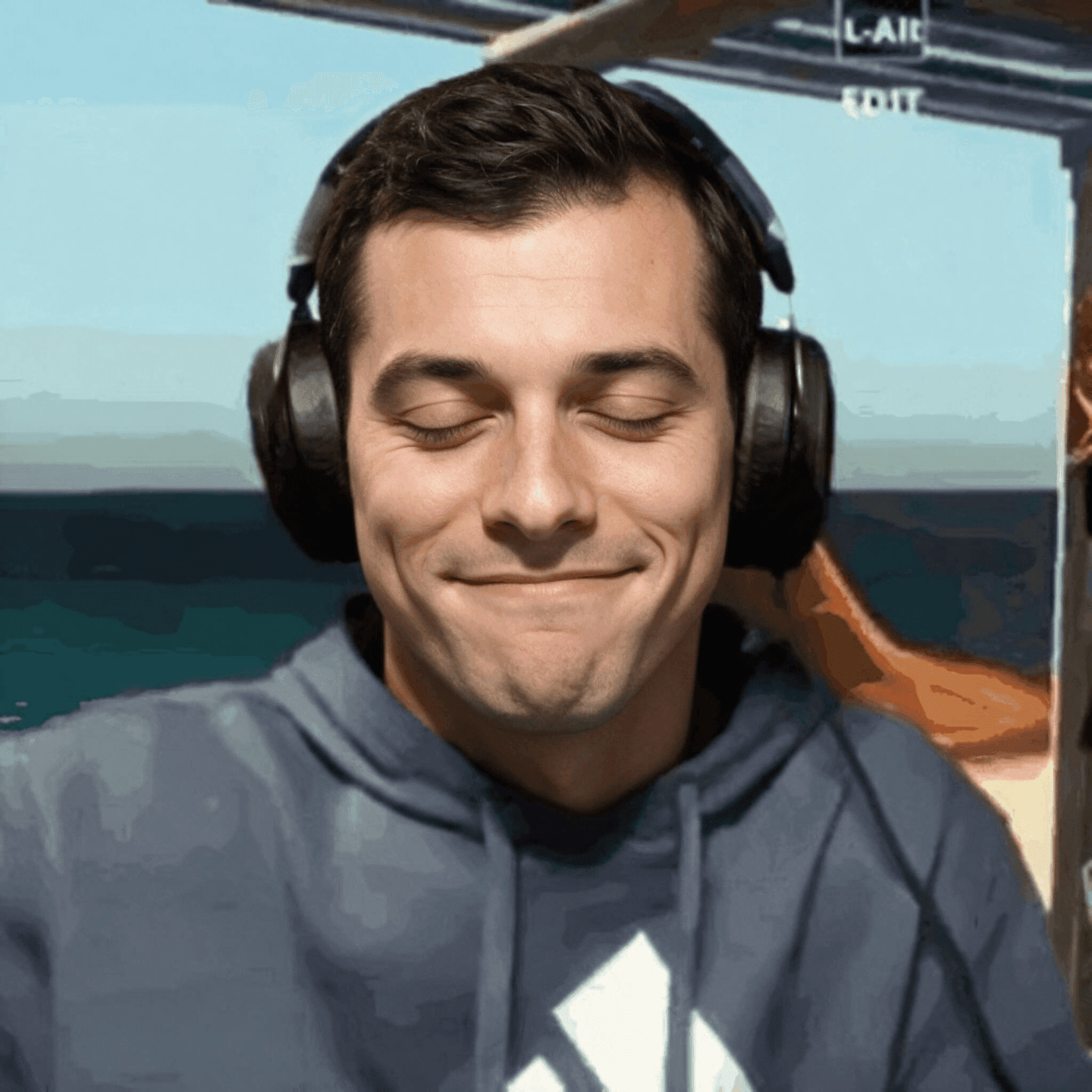 Smiling man with closed eyes wearing headphones by the ocean