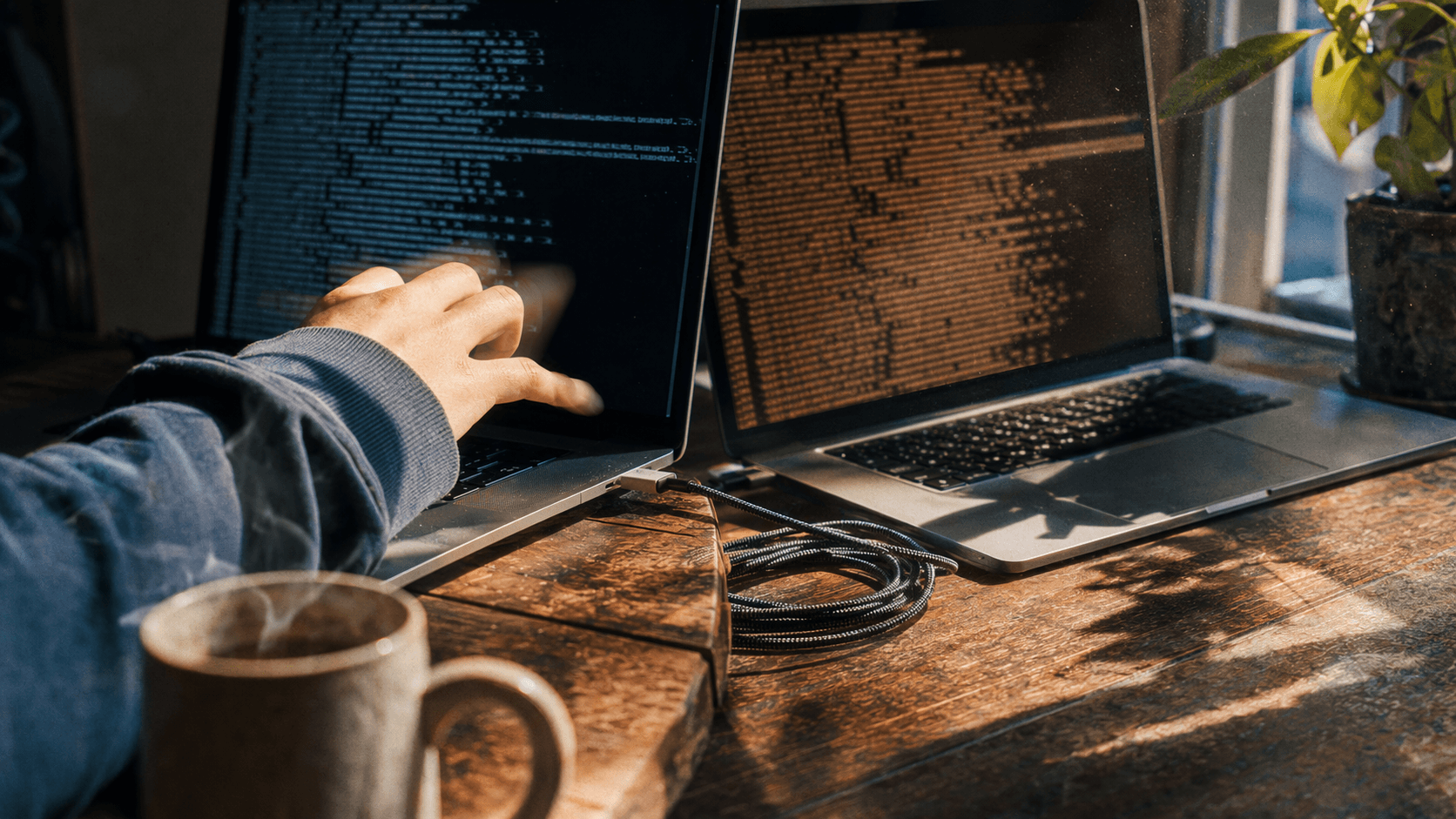 Hand typing on a laptop displaying code next to a coffee cup