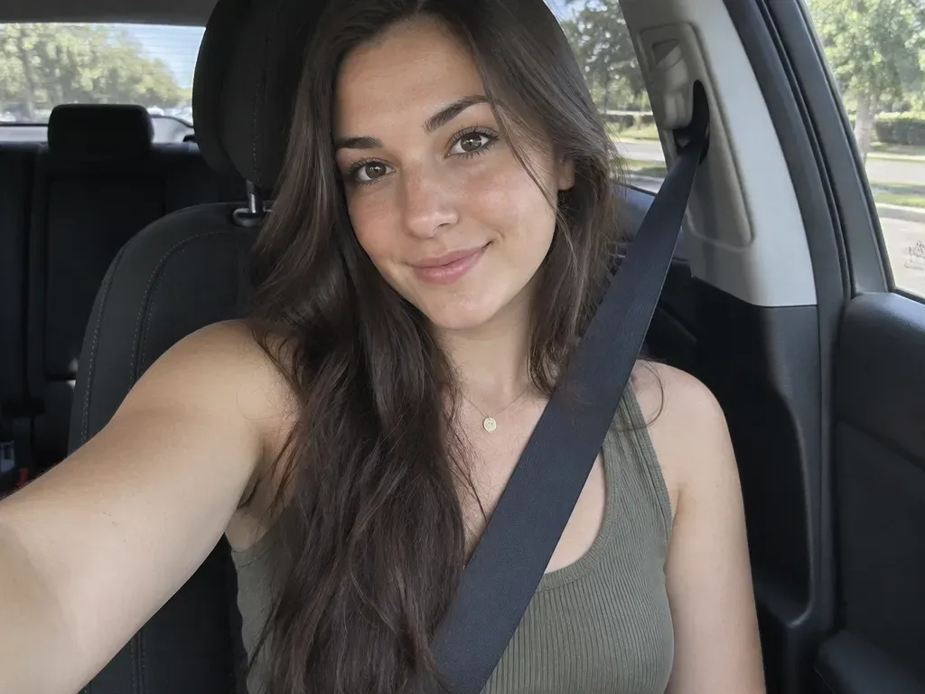 Photorealistic AI selfie generated with GPT Image 2.5 showing a young woman in a car driver seat with seatbelt and natural side-window lighting