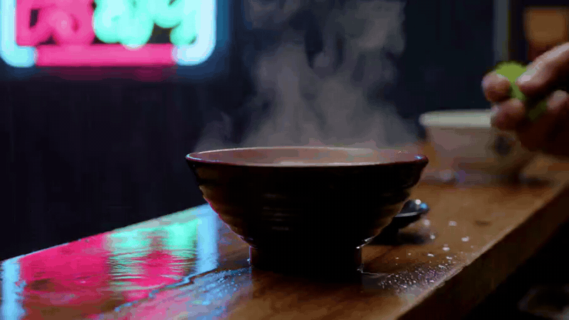 Steam rising from a bowl of soup on a wooden counter