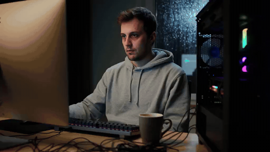 Man in grey hoodie staring at a glowing computer screen