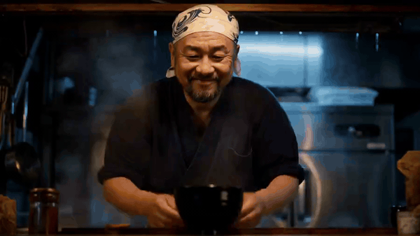 Smiling chef in a bandana serving a steaming bowl of food