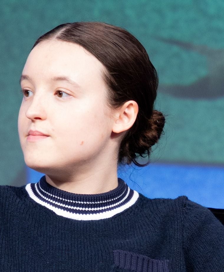 Bella Ramsey looking sideways in a blue sweater with a striped collar