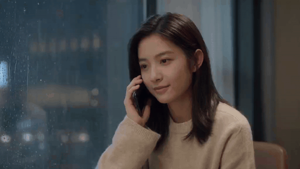 Donna sorridente al telefono accanto a una finestra piovosa
