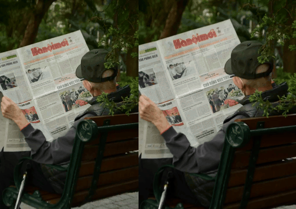 Man in a cap reading a Vietnamese newspaper on a park bench