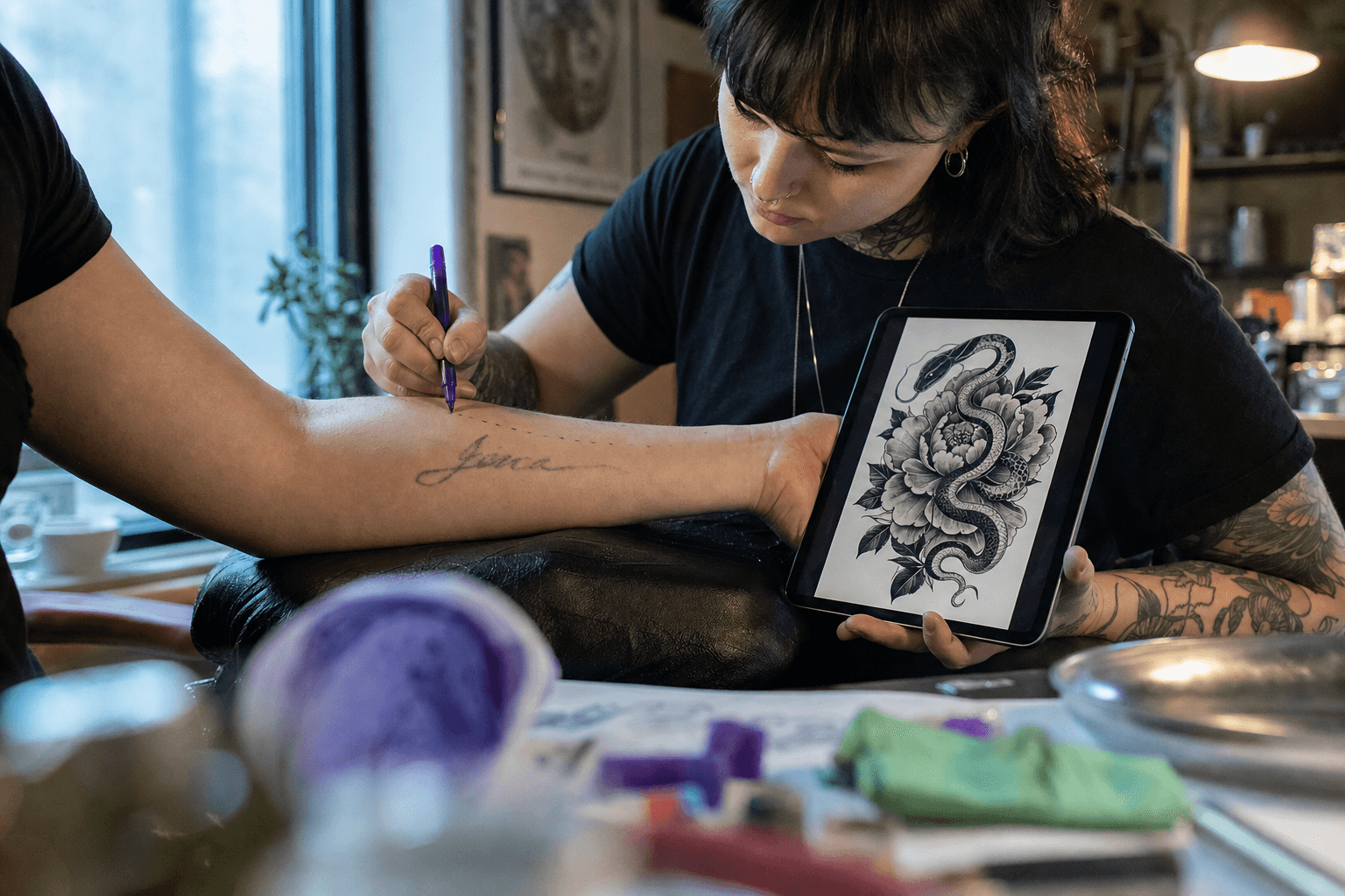 Tattoo artist draws on arm while holding tablet showing snake design