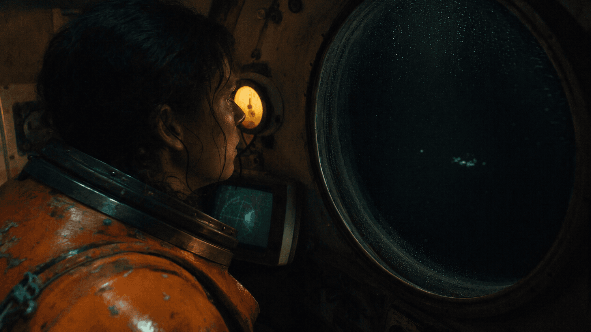 A person in an orange suit looks out a submarine porthole